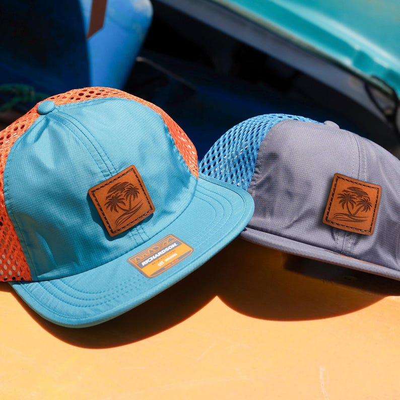 May include: Two mesh trucker hats with a palm tree logo on the front. The hat on the left is blue with orange mesh and the hat on the right is gray with blue mesh.