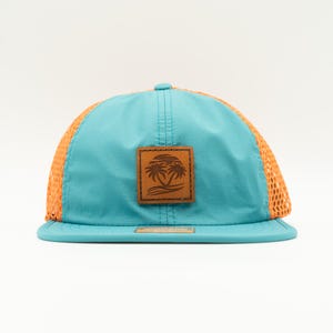 May include: A blue and orange mesh trucker hat with a brown leather patch featuring a palm tree design.