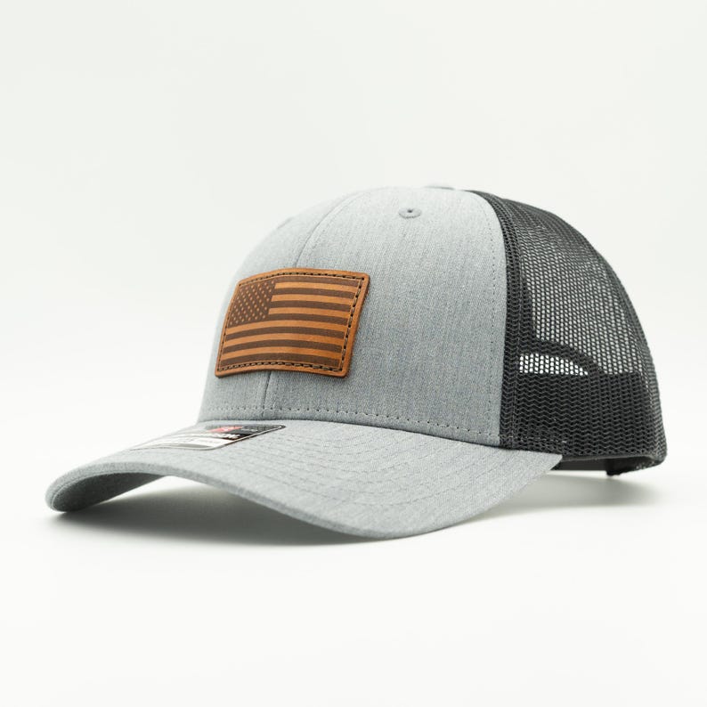 Add a patriotic touch to your look with our Grey and black Richardson 115 or 112 hat. Featuring a hand-sewn American flag leather patch, adjustable Snapback, and made in Colorado, USA for quality you can trust! Quality Trucker cap with mesh back.