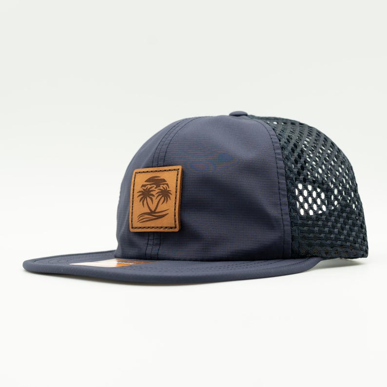 May include: A navy blue mesh back baseball cap with a brown leather patch featuring a palm tree design.