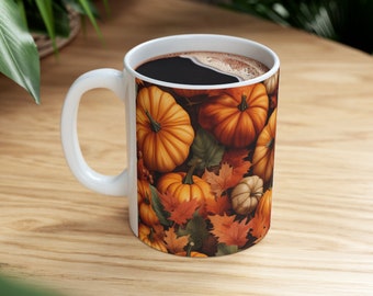 May include: White ceramic mug with a fall-themed design featuring orange and brown pumpkins and autumn leaves. The mug is filled with coffee.