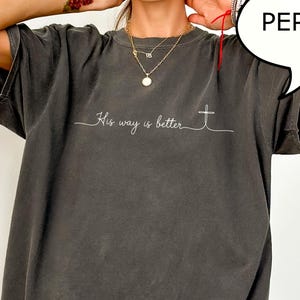 May include: Dark gray t-shirt with the text "His way is better" and a cross graphic. The shirt has a relaxed fit and short sleeves. The word "PEPPER" is in a speech bubble.