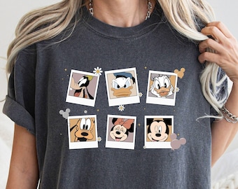May include: A dark gray t-shirt with a print of Disney characters in Polaroid frames. The characters include Mickey Mouse, Minnie Mouse, Donald Duck, Goofy, and Pluto. The print is surrounded by small white flowers and hearts.