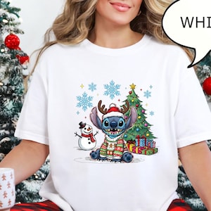 Puede incluir: Camiseta blanca de cuello redondo con un personaje de dibujos animados que lleva un jersey navide&ntilde;o, cuernos y un gorro de Pap&aacute; Noel. Tambi&eacute;n se representa un &aacute;rbol de Navidad, un mu&ntilde;eco de nieve y copos de nieve. La palabra "WHITE" est&aacute; en un bocadillo.