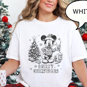 Puede incluir: Camiseta blanca con un gr&aacute;fico navide&ntilde;o de Mickey Mouse en blanco y negro, sosteniendo una bebida y un &aacute;rbol de Navidad. El texto "MERRY CHRISTMAS" est&aacute; debajo. Un bocadillo dice "WHITE".