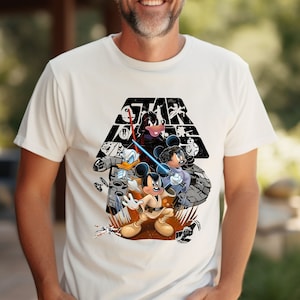 May include: White t-shirt with a black and white graphic of Mickey Mouse, Donald Duck, and Goofy dressed as Star Wars characters. The text "STAR WARS" is printed above the characters.