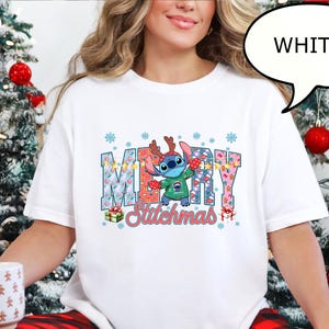 Op de afbeelding: Wit T-shirt met een kleurrijke afbeelding met het woord "MERRY" en "Stitchmas" met een stripfiguur met een kersttrui en rendiergewei. Het shirt wordt gecombineerd met een rood-zwarte geruite pyjamabroek.