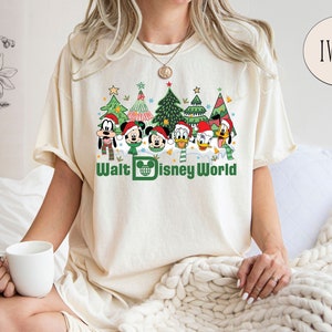 May include: A white t-shirt with a Christmas-themed design featuring Mickey Mouse and friends in front of Christmas trees. The text "Walt Disney World" is printed below the characters.
