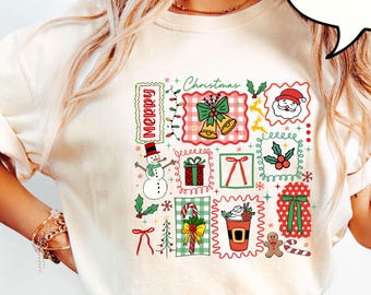May include: Ivory-coloured t-shirt with a Christmas design. The graphic includes a snowman, Santa, bells, gifts, and candy canes. The word "Merry" is vertically printed on the left. The shirt is made of a soft material.