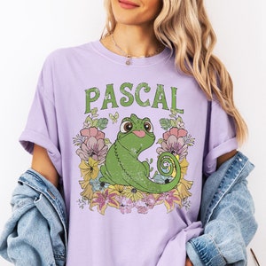 May include: A lavender t-shirt with a green chameleon cartoon character named Pascal surrounded by flowers. The text "PASCAL" is printed in green above the character.