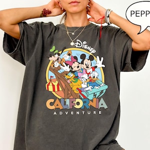 Puede incluir: Una camiseta gris oscuro con un estampado gr&aacute;fico de Mickey Mouse y sus amigos montando una monta&ntilde;a rusa. El texto "Disney California Adventure" est&aacute; impreso debajo del gr&aacute;fico.