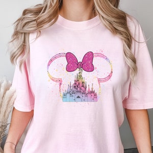 Puede incluir: Camiseta rosa con un dise&ntilde;o de acuarela de un castillo con un lazo rosa en la parte superior. El castillo est&aacute; rodeado de un dise&ntilde;o de acuarela rosa, azul y amarillo.