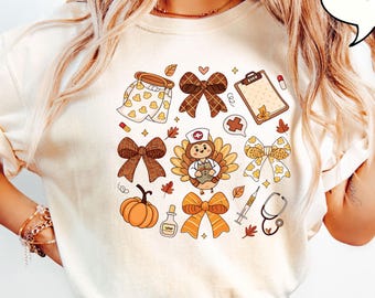 May include: Ivory-colored t-shirt featuring a Thanksgiving-themed graphic. The design includes a turkey wearing a nurse's hat, bows, pumpkins, and autumn leaves. The word "IVORY" is in a speech bubble.