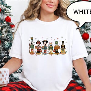May include: White crew neck t-shirt featuring a colorful graphic of Disney characters dressed as nutcrackers. The characters include Mickey Mouse, Minnie Mouse, Donald Duck, and Goofy. The word "WHITE" is in a speech bubble.