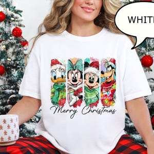 Puede incluir: Camiseta blanca con Donald Duck, Minnie Mouse, Mickey Mouse y Goofy con atuendos navide&ntilde;os. Las palabras "Merry Christmas" est&aacute;n escritas debajo de los personajes. La camiseta forma parte de un tema navide&ntilde;o.