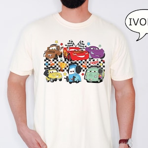 May include: A white t-shirt with a checkered pattern and a graphic of cartoon cars. The cars are red, blue, green, purple, and brown. The text "Cars" is on the shirt.