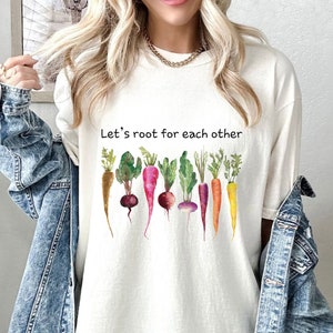 May include: White t-shirt with the text "Let's root for each other" and a watercolor illustration of a row of colorful carrots and turnips.