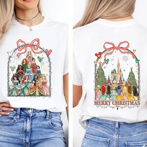 May include: White t-shirt with a colourful graphic of Disney princesses under a pink bow and Mickey Mouse balloons. The back of the shirt shows the princesses in front of a castle with the words "Merry Christmas".