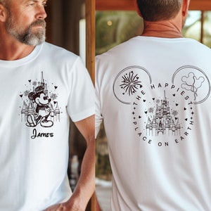 K&ouml;nnte beinhalten: Wei&szlig;es T-Shirt mit einer Schwarz-Wei&szlig;-Illustration von Mickey Mouse vor einem Schloss und dem Namen "James" darunter. Auf der R&uuml;ckseite des Shirts steht der Text "The Happiest Place on Earth."