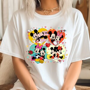 Puede incluir: Camiseta blanca con un estampado gr&aacute;fico colorido de Mickey Mouse y Minnie Mouse en varias poses. El gr&aacute;fico presenta corazones, flores y otros detalles rom&aacute;nticos.