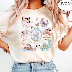 Puede incluir: Camiseta de color marfil con gr&aacute;ficos coloridos de personajes de Disney. El dise&ntilde;o incluye Mickey y Minnie Mouse, un castillo y el texto "BEST DAY EVER". Otros gr&aacute;ficos incluyen una taza de t&eacute;, un barco y un pretzel.