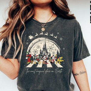 Puede incluir: Una camiseta gris oscuro con un gr&aacute;fico de estilo vintage de Mickey Mouse y sus amigos caminando por un paso de cebra frente al Castillo de Cenicienta en Disney World. El gr&aacute;fico incluye el texto "The most magical place on Earth".
