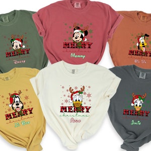 Op de afbeelding: Zes verschillende T-shirts met een kerstthema met Mickey Mouse, Donald Duck en Goofy. Elk shirt heeft een andere naam, waaronder "Daddy", "Mommy", "Big Sis", "Lil Bro", "Aldo" en "Julie".