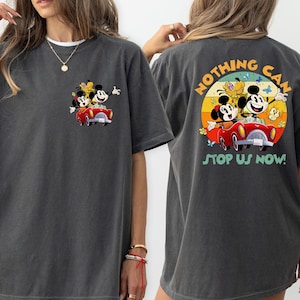 以下が含まれることがあります： グレーのオーバーサイズTシャツ。ヴィンテージなミッキーマウス、ミニーマウス、プルートが赤い車に乗っているカートゥーン画像がプリントされています。Tシャツの背面には「Nothing Can Stop Us Now!」というテキストと、車に乗っているキャラクターの同様のヴィンテージなカートゥーン画像がプリントされています。