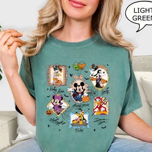 Puede incluir: Una camiseta verde claro con ilustraciones enmarcadas de personajes de Disney con disfraces de Halloween. Los personajes incluyen Mickey Mouse, Minnie Mouse, Donald Duck, Goofy y Pluto. La camiseta tiene el texto "Mickey Mouse" y "Minnie Mouse".