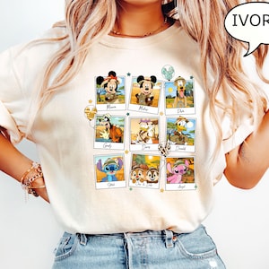 Puede incluir: Una camiseta blanca con un collage de personajes de Disney con atuendos de safari. Los personajes incluyen a Mickey Mouse, Minnie Mouse, Pluto, Goofy, Daisy Duck, Donald Duck, Stitch, Chip, Dale y Angel. La camiseta tiene un color marfil claro.
