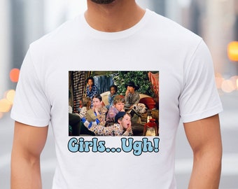 May include: White t-shirt with a printed image of a group of children sitting in a cabin. The image is surrounded by a black border. The text "Girls... Ugh!" is printed in blue below the image.