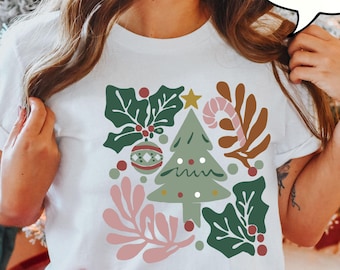 Puede incluir: Camiseta blanca con un diseño navideño festivo. El gráfico incluye un árbol de Navidad verde, acebo, adornos y un bastón de caramelo. La palabra "WHITE" está en una burbuja.