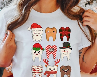 Op de afbeelding: Wit T-shirt met een raster van negen cartoon tanden met kerstthema's. Elke tand is versierd als de kerstman, peperkoek, een ingepakt cadeau, een elf, beugels, een sneeuwman, zuurstok, rendier en peperkoek.
