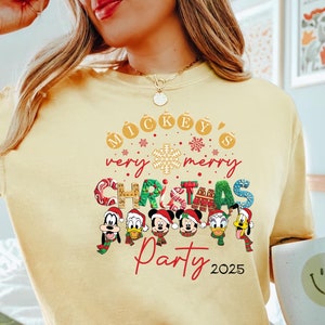 K&ouml;nnte beinhalten: Ein gelbes Langarmshirt mit einem Weihnachtsmotiv mit Mickey Mouse und seinen Freunden. Das Shirt sagt "Mickey's Very Merry Christmas Party 2025".