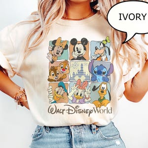 May include: Ivory-colored t-shirt featuring a grid of Disney characters including Mickey Mouse, Minnie Mouse, Goofy, Donald Duck, and Stitch. The words "Walt Disney World" are printed in a stylized font below the grid.