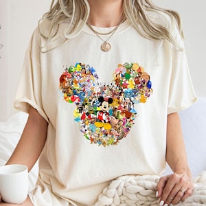 May include: A white t-shirt with a graphic of Mickey Mouse's ears made up of various Disney characters. The characters include Mickey Mouse, Minnie Mouse, Donald Duck, Goofy, Pluto, and many more.