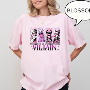 May include: A light pink t-shirt featuring a graphic of four cartoon villains with bubblegum. The text "Sweetie I'm OK with being the Villain" is printed below the characters in purple. A speech bubble says "BLOSSOM".