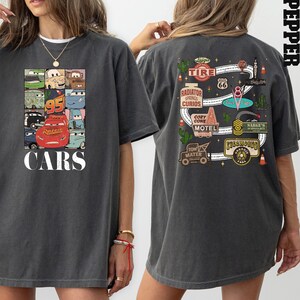 Puede incluir: Una camiseta de gran tama&ntilde;o de color gris oscuro con un gr&aacute;fico tem&aacute;tico de Cars en la parte delantera y un gr&aacute;fico tem&aacute;tico de la Ruta 66 en la parte posterior. El gr&aacute;fico delantero presenta un collage de personajes de Cars, incluidos Rayo McQueen, Mate y otros. El gr&aacute;fico trasero presenta un mapa de Radiador Springs con varios puntos de referencia y negocios.