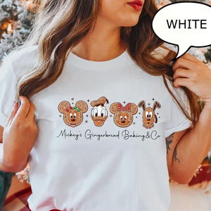 Puede incluir: Camiseta blanca con dise&ntilde;os de personajes de pan de jengibre de Mickey, Donald, Minnie y Pluto. El texto "Mickey's Gingerbread Baking & Co." est&aacute; escrito en cursiva debajo de los personajes. Una burbuja de di&aacute;logo con la palabra "WHITE" est&aacute; en la esquina superior derecha.