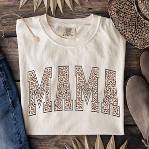May include: A cream colored t-shirt with a leopard print "MAMA" graphic.