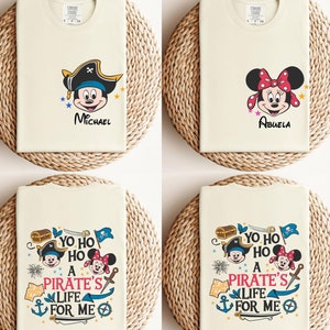 May include: Four white t-shirts with different designs featuring Mickey Mouse and Minnie Mouse. The shirts have the text "Yo ho ho a pirate's life for me" and the names "Michael" and "Abuela".