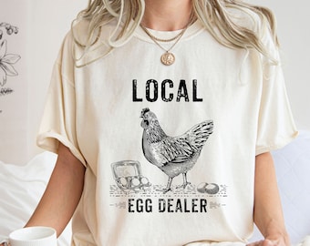 May include: A white t-shirt with a black graphic of a chicken and the text "LOCAL EGG DEALER".