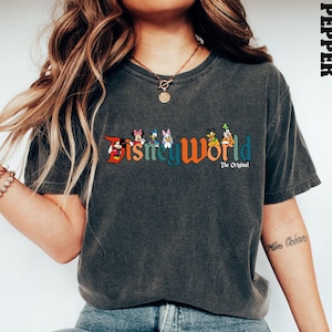 K&ouml;nnte beinhalten: Ein dunkelgraues T-Shirt mit einer Vintage-Grafik "Disney World", die Mickey Mouse, Minnie Mouse, Donald Duck, Goofy und Pluto zeigt. Der Text "The Original" ist unter der Grafik gedruckt.