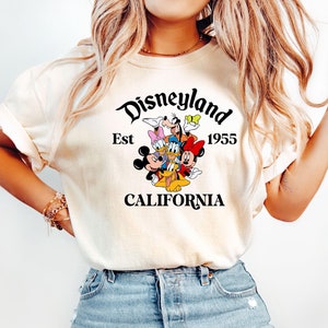 Puede incluir: Una camiseta blanca con un gr&aacute;fico negro de Mickey Mouse y sus amigos. El gr&aacute;fico dice "Disneyland Est 1955 California".