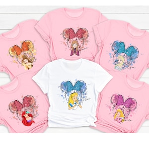 Peut inclure: Six t-shirts roses et blanches avec un motif aquarelle de princesses Disney avec des oreilles de souris. Chaque t-shirt a une princesse diff&eacute;rente et le nom "Anna", "Elsa", "Ariel", "Belle", "Alice" et "Aurora" est &eacute;crit sur chaque t-shirt.