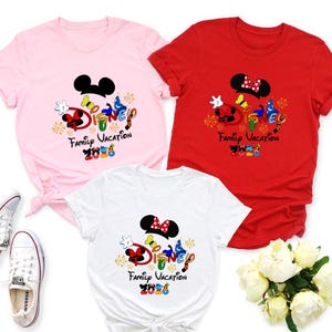 May include: Three short-sleeved t-shirts in pink, red, and white, each featuring a Disney-themed graphic. The graphic includes Mickey and Minnie Mouse ears, the word "Disney" in colorful letters, and the text "Family Vacation 2023".