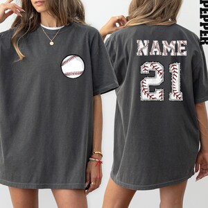 Könnte beinhalten: Ein übergroßes T-Shirt in Anthrazitgrau mit einem Baseball-Motiv auf der Vorderseite und einer Baseball-Nummer "21" sowie dem Wort "NAME" auf der Rückseite.