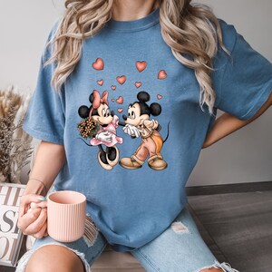 May include: A blue t-shirt with a graphic of Mickey Mouse and Minnie Mouse holding hands.  There are red hearts scattered around them.