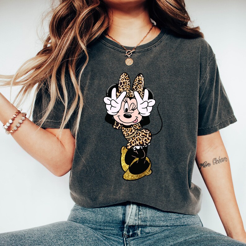 K&ouml;nnte beinhalten: Dunkelgraues T-Shirt mit Minnie Mouse im Leopardenmuster, die ein Friedenszeichen zeigt. Das T-Shirt hat einen Vintage-Wasch-Look.