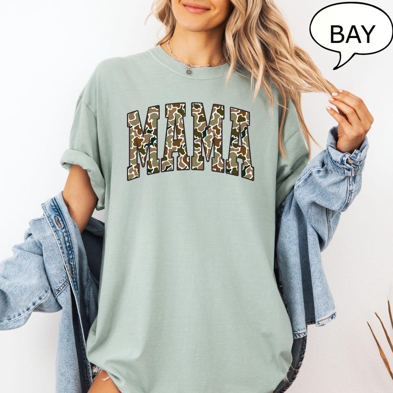 May include: A light green t-shirt with a camouflage print of the word "MAMA" in a collegiate font.